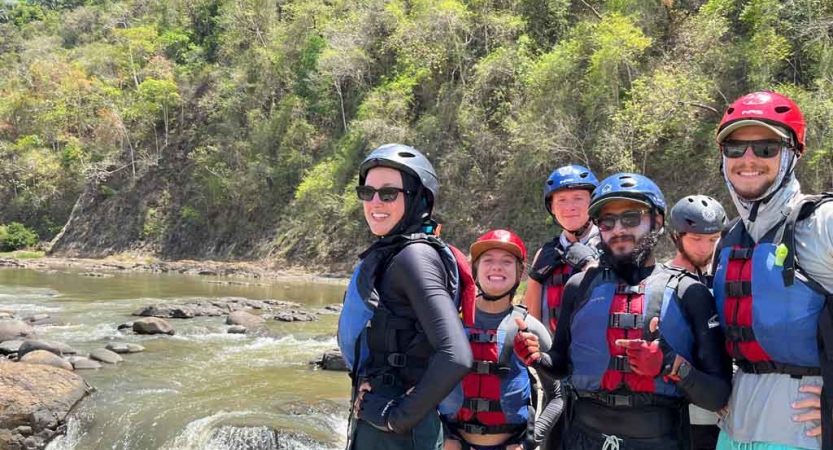 a group of gap year students wear whitewater gear and stand on the edge of a river